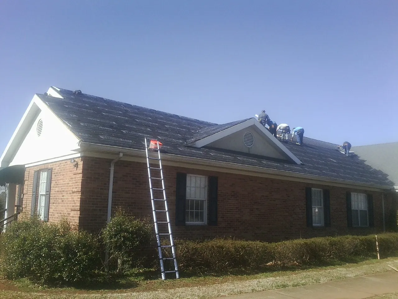 Crew tearing shingles off a brick ranch roof with a ladder set — Metal Roof Repair work by our crew in Winfield